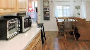 A kitchen with wooden cabinets, a double toaster oven, and a dining area with a wooden table and chairs. - Casita (Prescott)