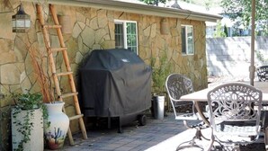 A patio with a stone wall, a barbecue grill, outdoor furniture, and a ladder leaning against the wall. - Casita (Prescott)