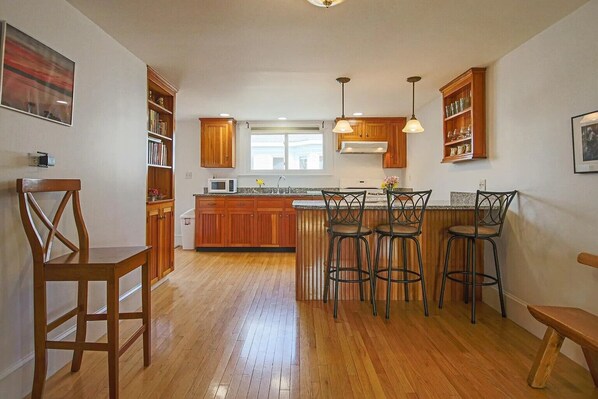 A spacious kitchen with wooden cabinets, a central island with bar stools, and pendant lighting. - Portland’s Best Ocean Views from a 40-Foot Private Deck (Portland)
