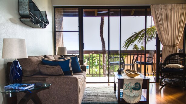 Ein Wohnzimmer mit Sofa, Couchtisch und Blick auf einen Balkon mit Gartenmöbeln.