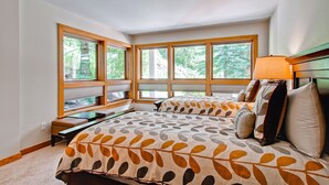 Un dormitorio con dos camas, ventanas amplias, un banco y una lámpara.