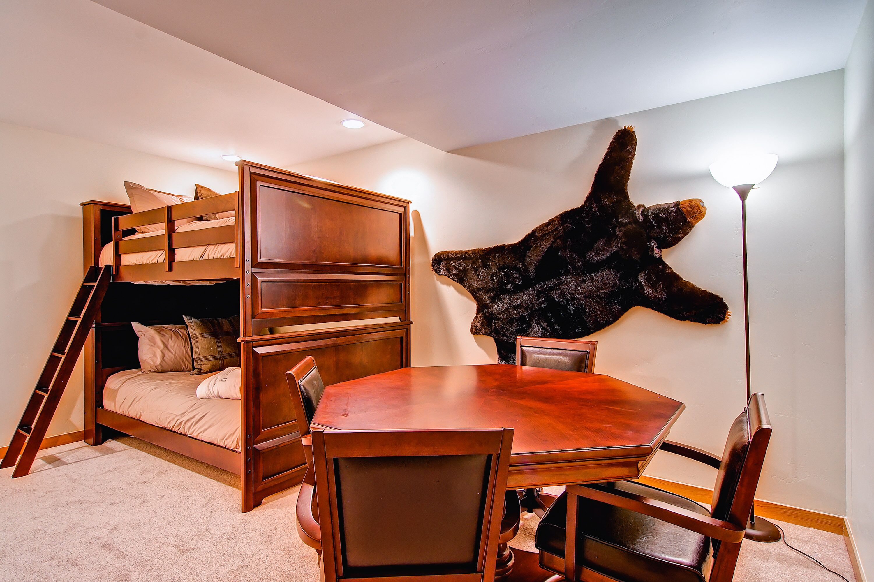 A room with a bunk bed, a dining table with chairs, and a mounted animal head on the wall.
