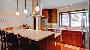 Una cocina moderna con una isla central, armarios de madera, electrodomésticos de acero inoxidable e iluminación colgante.