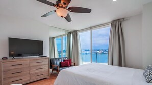 Hotelkamer met een groot bed, een televisie op een houten dressoir, een stoel en uitzicht op de stad en het water.