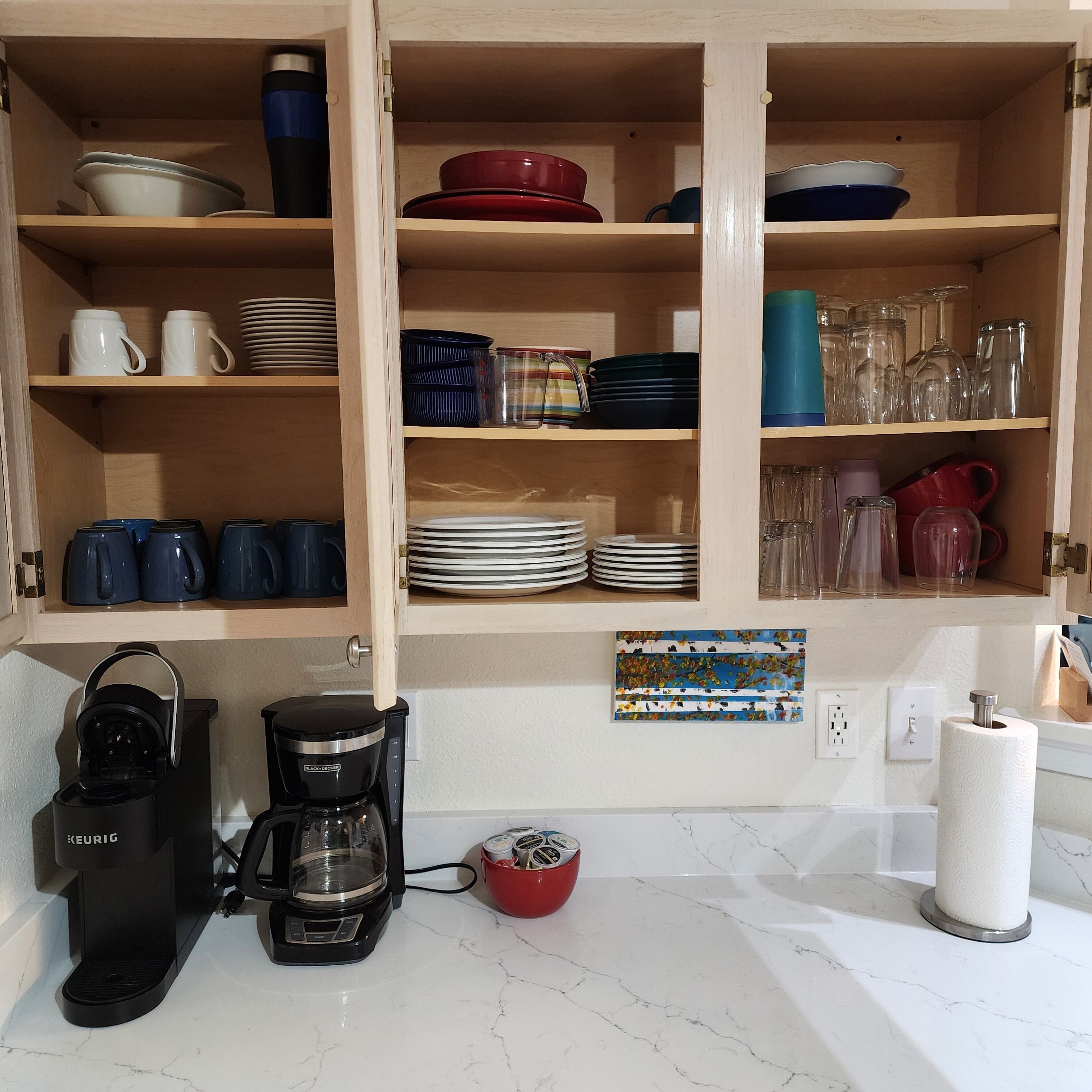 Une cuisine avec des meubles en bois, une machine à café, ainsi que divers plats et tasses.