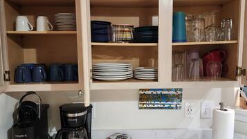 Une cuisine avec des meubles en bois, une machine à café, ainsi que divers plats et tasses.