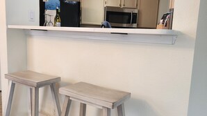 A kitchen with a white countertop, two wooden stools, and a sign that reads "IT'S WINE O'CLOCK".