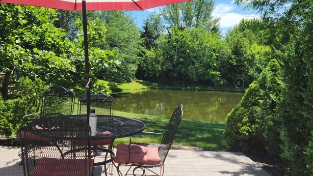 A deck with a table and chairs, an umbrella, and a view of a lake surrounded by trees.