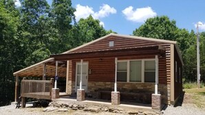 A wooden cabin with a porch, stone foundation, and a bench.