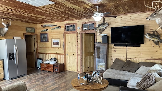 A cozy living room with a wooden ceiling, a ceiling fan, a large flat-screen TV, a sofa, and a coffee table.