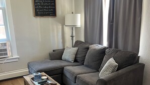 Un salon comprenant un canapé d’angle, une table basse en bois, un tapis à motifs, une lampe et une citation inspirante affichée sur le mur.