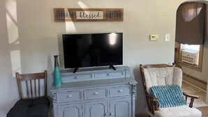A living room with a flat-screen TV on a dresser, a chair with a cushion, and a wall-mounted sign.