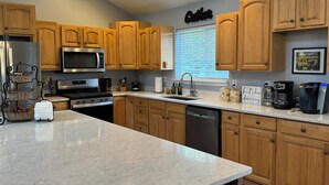 A modern kitchen with wooden cabinets, stainless steel appliances, and a marble countertop. - Country escape next to town for a quaint cottage getaway & majestic Rainer view (Yelm)