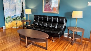 A room with a black leather sofa, two round wooden tables, a wooden coffee table, a blue wall, and a framed painting. - West Inn on Weston - Great for Families (Niagara Falls)
