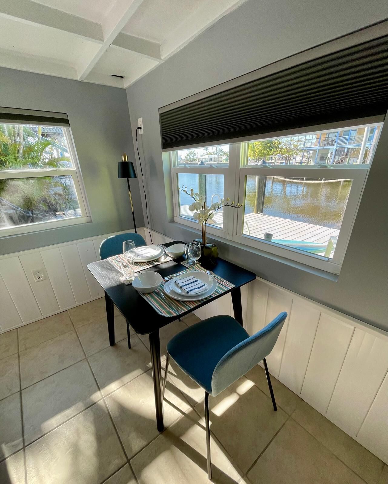 A dining area with a table set for two, a view of a water body outside, and a window with blinds.