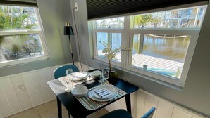 Een eetgedeelte met een tafel voor twee personen, uitzicht op een wateroppervlak en een raam met jaloezieën.