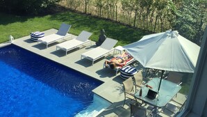 A swimming pool with lounge chairs and a table with a laptop.