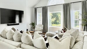 A modern living room with a large sectional sofa, a flat-screen TV mounted on the wall, and a ceiling fan.