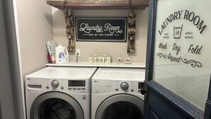 A laundry room with two front-loading LG washers, a soap dispenser, and a sign above the washers.
