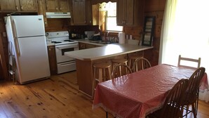A kitchen with wooden cabinets, a refrigerator, stove, and a dining area with a table and chairs. - Lake Lovers Lodge Dale Hollow Lake Allons TN Near Willow Grove/Lily Dale Resorts (Allons)
