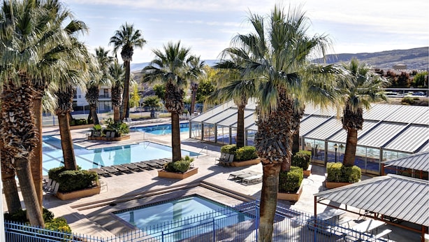 Zona de piscina en un resort con palmeras, sillas de descanso y una vista despejada del paisaje circundante.