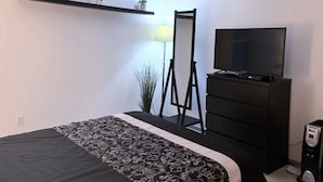 Une chambre à coucher comprenant un lit, une commode, un téléviseur et un bureau avec un ordinateur.