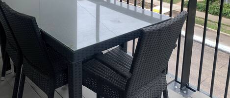 En balkon med et bord og stole, med udsigt over en gade med bygninger og parkerede biler.