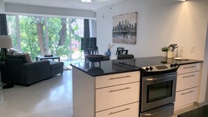 Une cuisine moderne avec des meubles blancs, un plan de travail noir et des appareils en acier inoxydable. On y trouve un coin repas avec une chaise noire et un canapé.