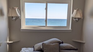 A bedroom with a bed, two wall-mounted lamps, a window with a view of the sea, and a small shelf above the bed. - Beautiful Gulf Front Unit with Balcony (Gulf Shores)