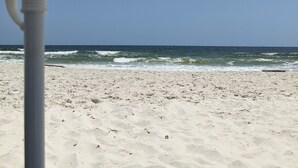 A beach with a white umbrella and a pole, sandy beach, and ocean waves. - Beautiful Gulf Front Unit with Balcony (Gulf Shores)