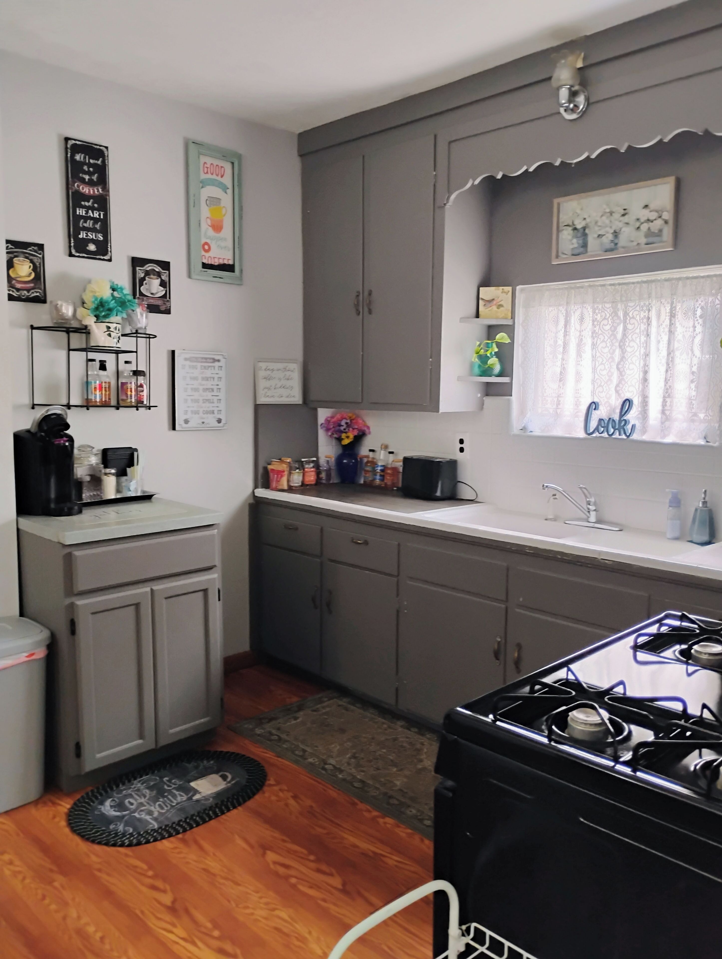 Une cuisine compacte avec des meubles gris, une cuisinière noire et une fenêtre sur laquelle est affiché un panneau indiquant « Cuisine ».