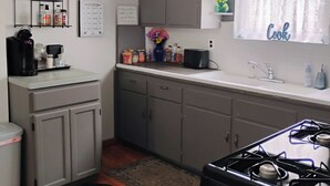 Une cuisine compacte avec des meubles gris, une cuisinière noire et une fenêtre sur laquelle est affiché un panneau indiquant « Cuisine ».