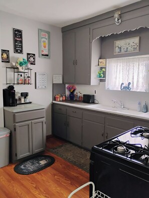 A compact kitchen with grey cabinets, a black stove, and a window with a 'Cook' sign.