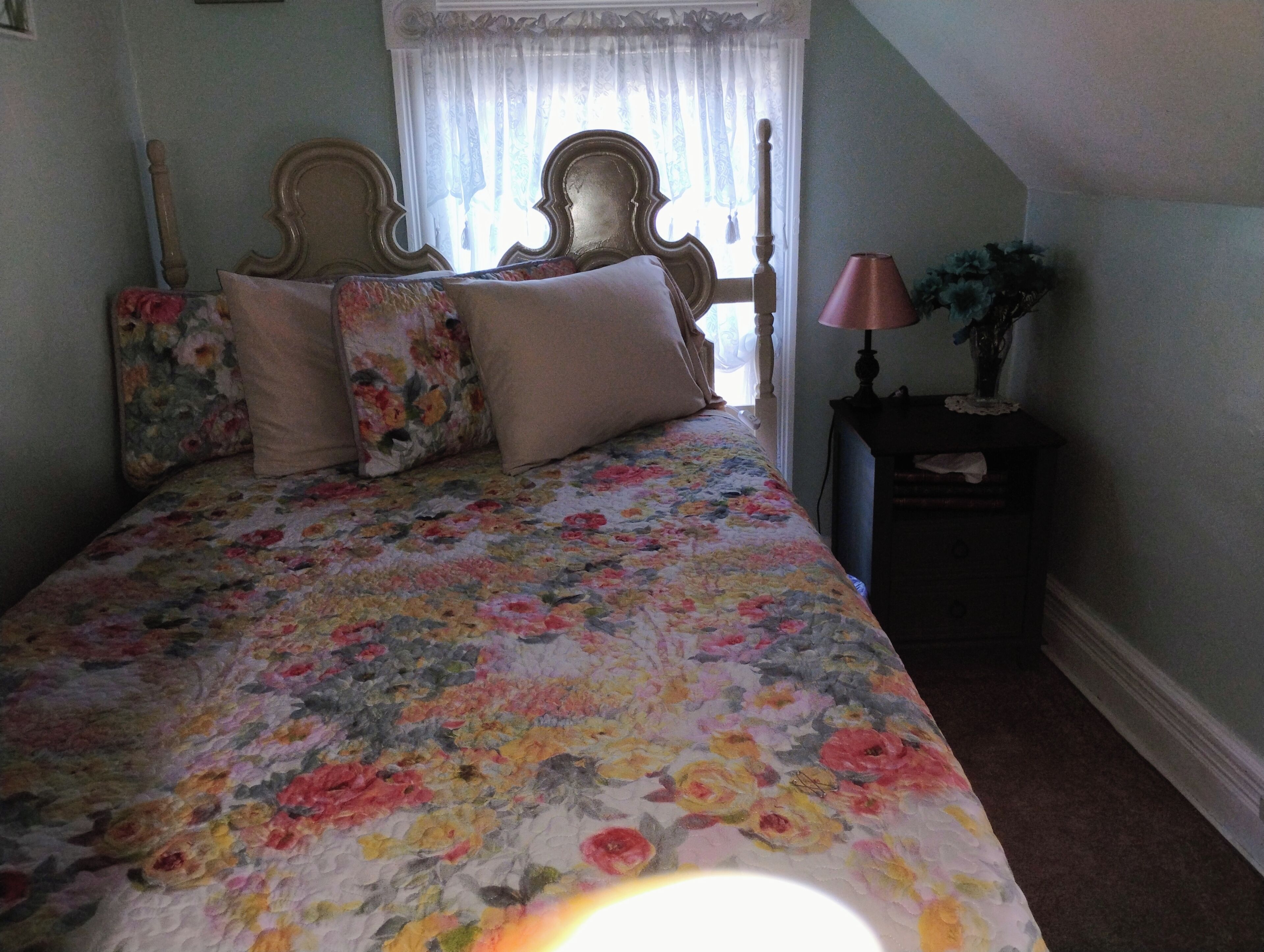 Een slaapkamer met een bloemenprint beddeken, een houten hoofdbord en een nachtkastje met een lamp.