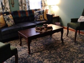 A living room with a dark sofa, a coffee table with a floral arrangement, and a patterned rug.