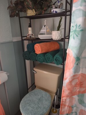 Een badkamer met toilet, een plank met opgerolde handdoeken en een douchegordijn.