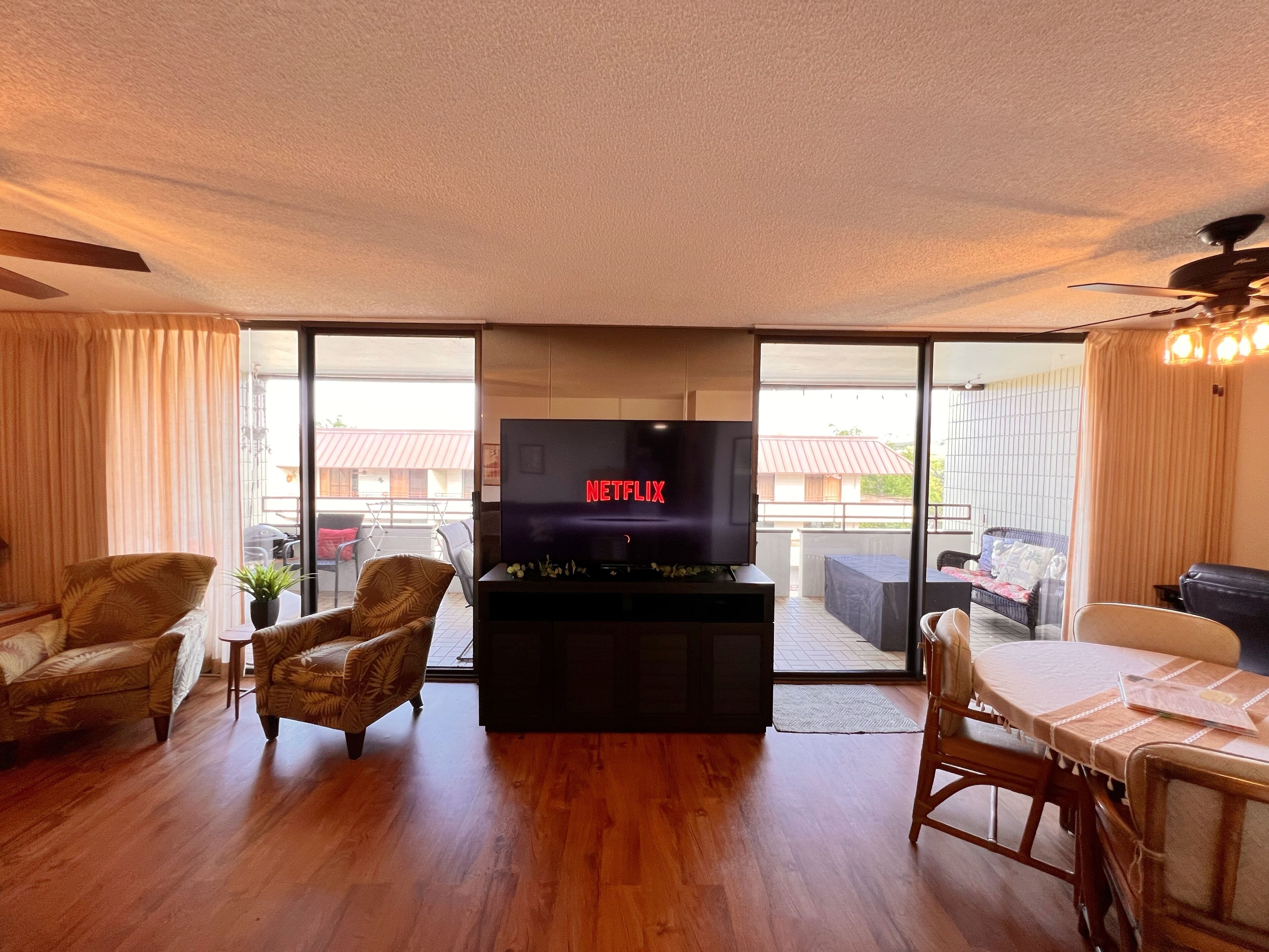 A living room with a flat-screen TV, wooden flooring, and a balcony with a view.