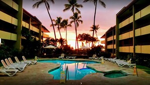 A pool area with lounge chairs, palm trees, and buildings in the background.