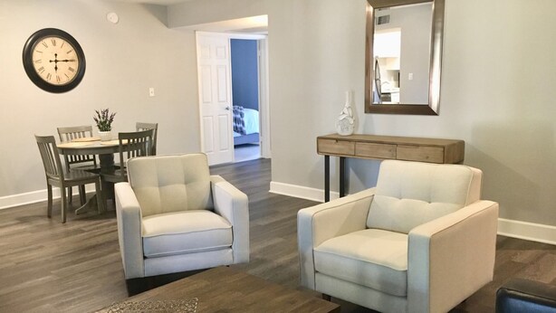 A living room with two armchairs, a dining table with chairs, a clock, and a console table with a mirror. - Stunning,  2 Bedroom Condo In Central Scottsdale at McCormick Ranch. (Scottsdale)