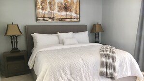 A neatly made bed with a white duvet and pillows, flanked by two bedside tables with lamps, in a room with a light blue wall and a landscape painting above the bed. - Stunning,  2 Bedroom Condo In Central Scottsdale at McCormick Ranch. (Scottsdale)