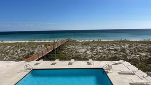Un espace piscine doté d’une terrasse en bois donnant sur la plage, le tout entouré de dunes de sable.