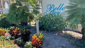 Une enseigne indiquant « Belle Her », avec le numéro « 8269 » inscrit au-dessus, le tout entouré d’une végétation luxuriante et de palmiers.