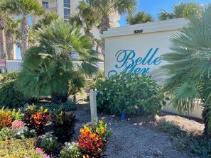 A sign for "Belle Her" with a number "8269" above it, surrounded by lush greenery and palm trees. - Belle Mer 203 - FREE BEACH SETUP March-October! (Navarre Beach)