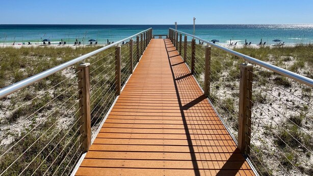 Une promenade en bois qui mène à une plage, avec un ciel bleu dégagé.