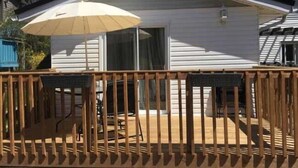 Une maison mobile de plain-pied dotée d’une terrasse, de meubles d’extérieur et d’un grand parasol.