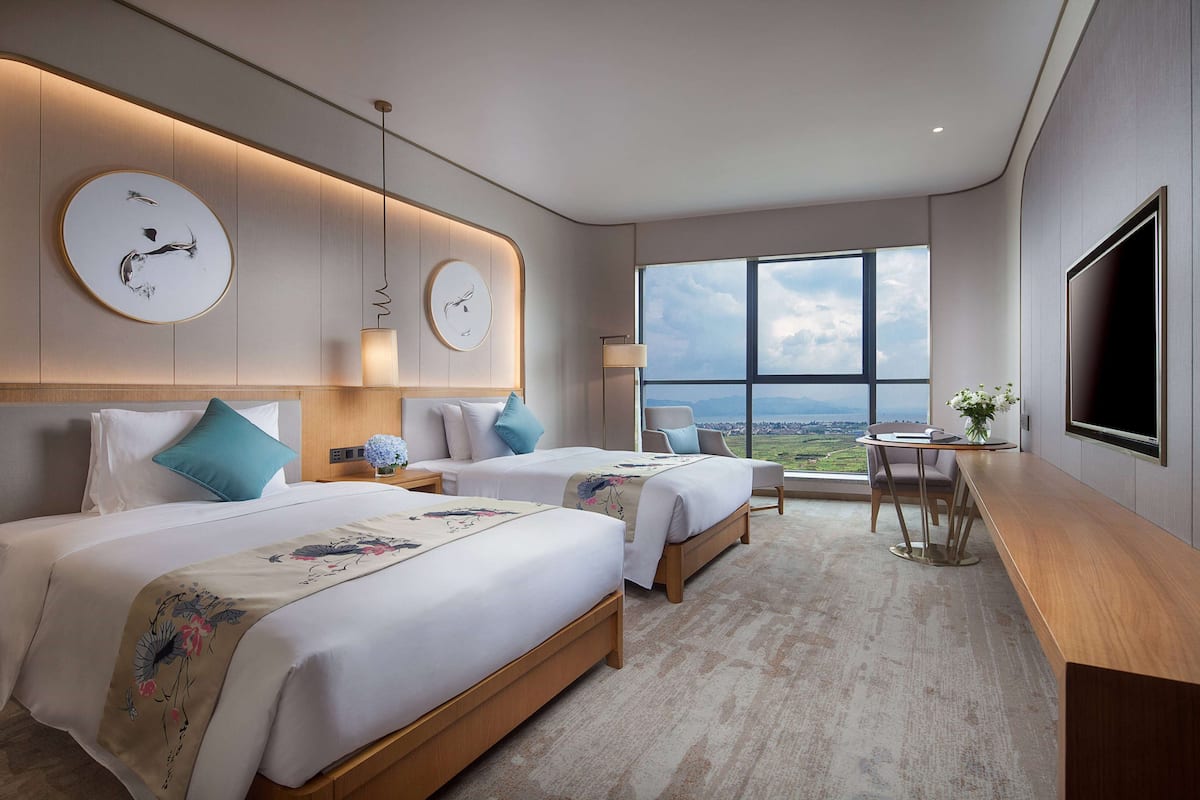 Een moderne hotelkamer met twee bedden, een groot raam en een flatscreen televisie.