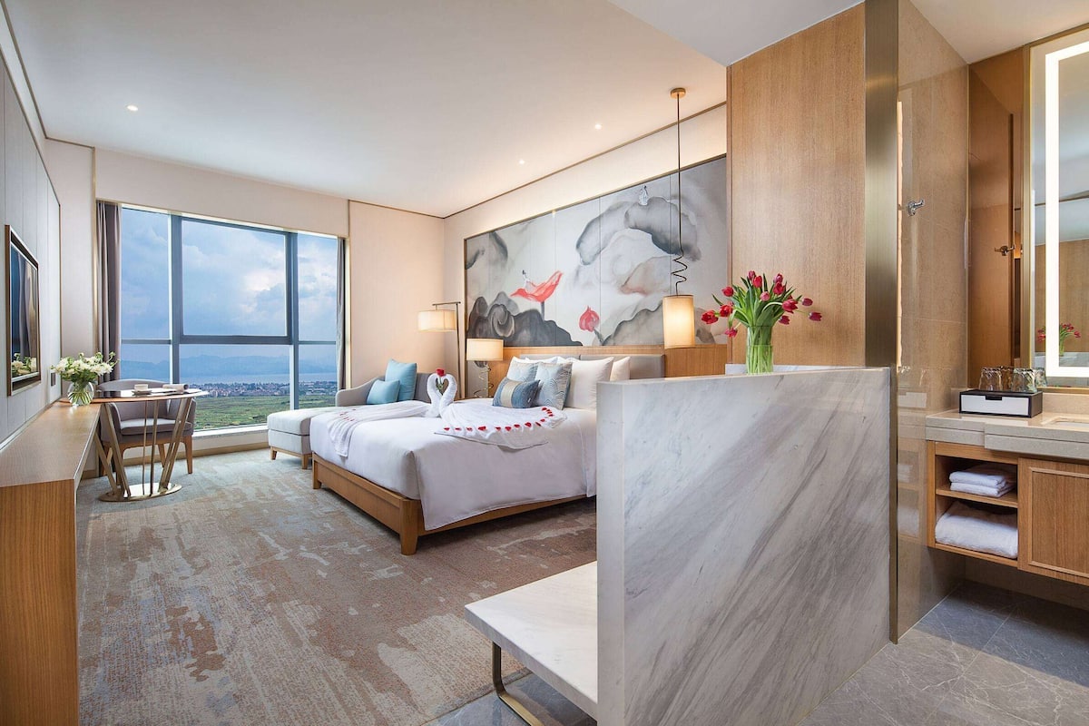 Een moderne hotelkamer met een groot bed, een bureau en uitzicht op de stad.