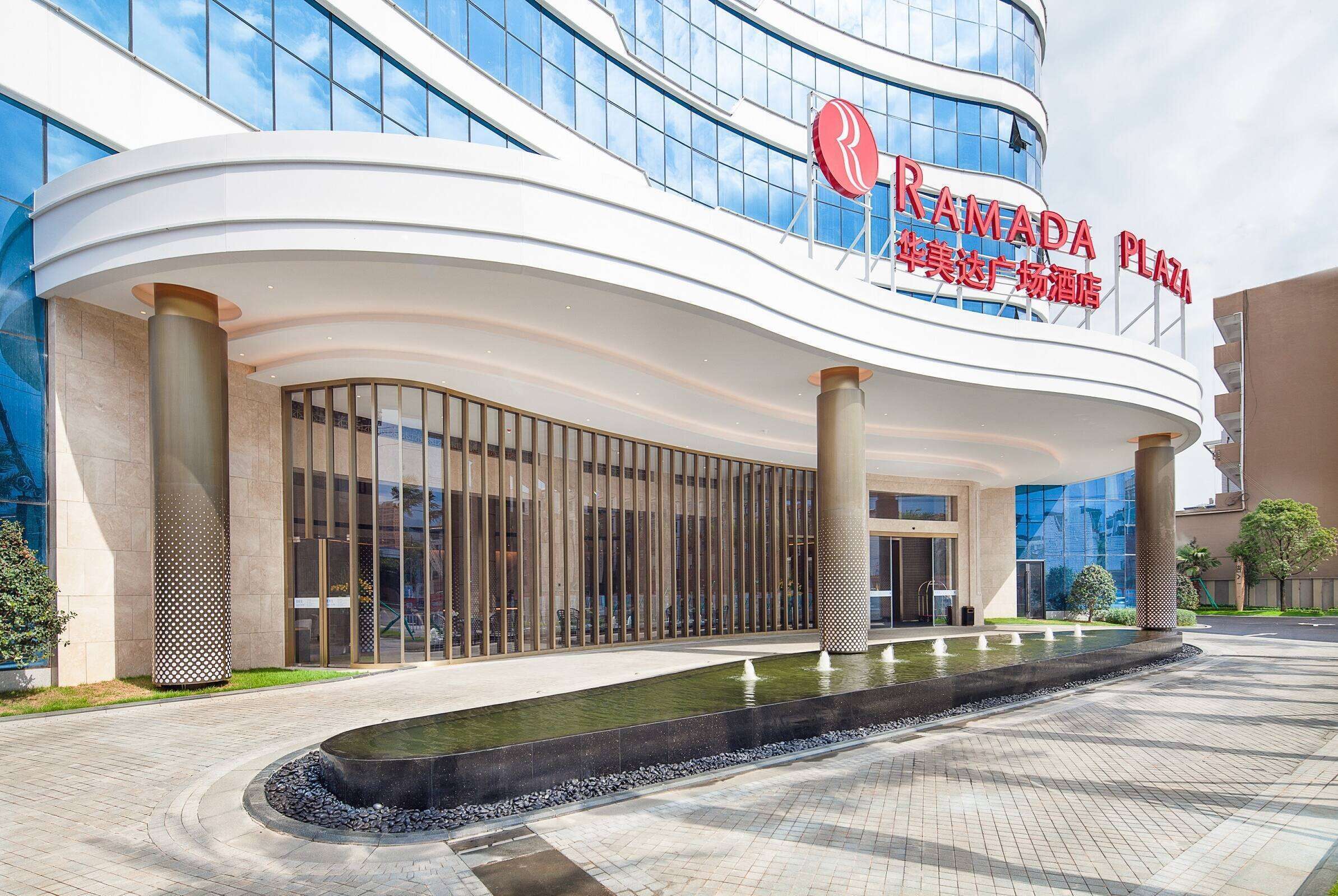 A modern building with a curved facade, large glass windows, and a sign reading "RAMADA PLAZA."