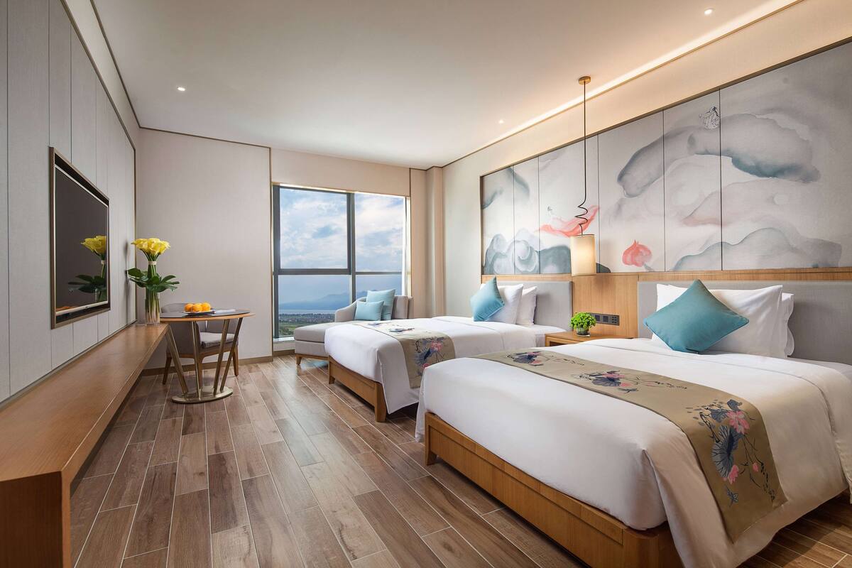 Een moderne hotelkamer met twee bedden, een eettafel en een groot raam met uitzicht.