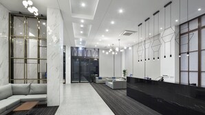 A modern reception area with a marble reception desk, a seating area with sofas, and a geometric light fixture. - Gangneung City Hotel (Gangneung)